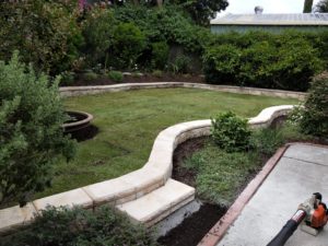 Retaining Wall, Light colored block retaining wall. curving around a lower level garden bed, with a step up to the upper level.